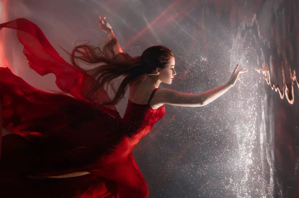 fairytale princess floating in dream dark water in red flowy dress