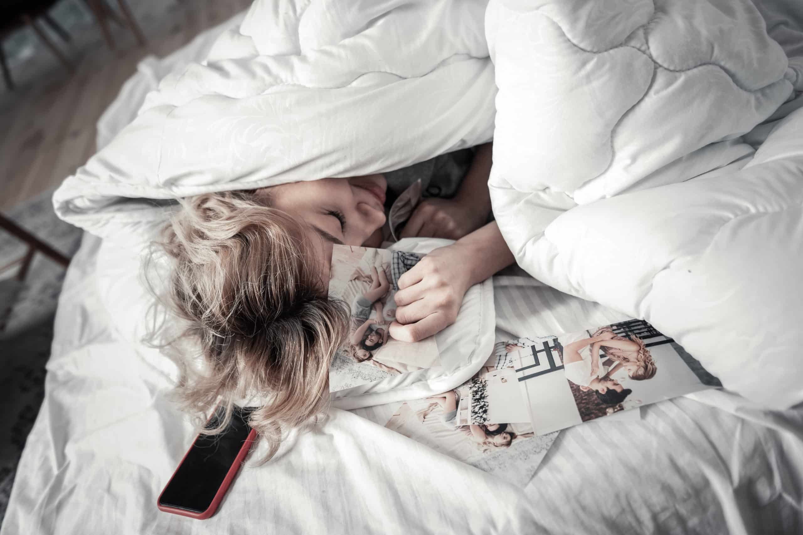 Young woman lying under blanket with photos with ex boyfriend