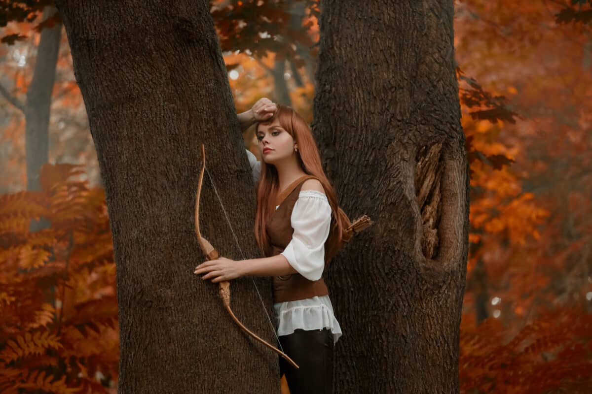 mysterious girl with bright red hair between the trees in autumn woods, charming hunter with bow and arrows behind her back, elf archer thoughtfully watching forest animals, kitsune in human form