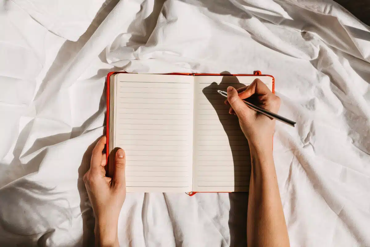 Hands holding an open blank notebook and a pen on bed background