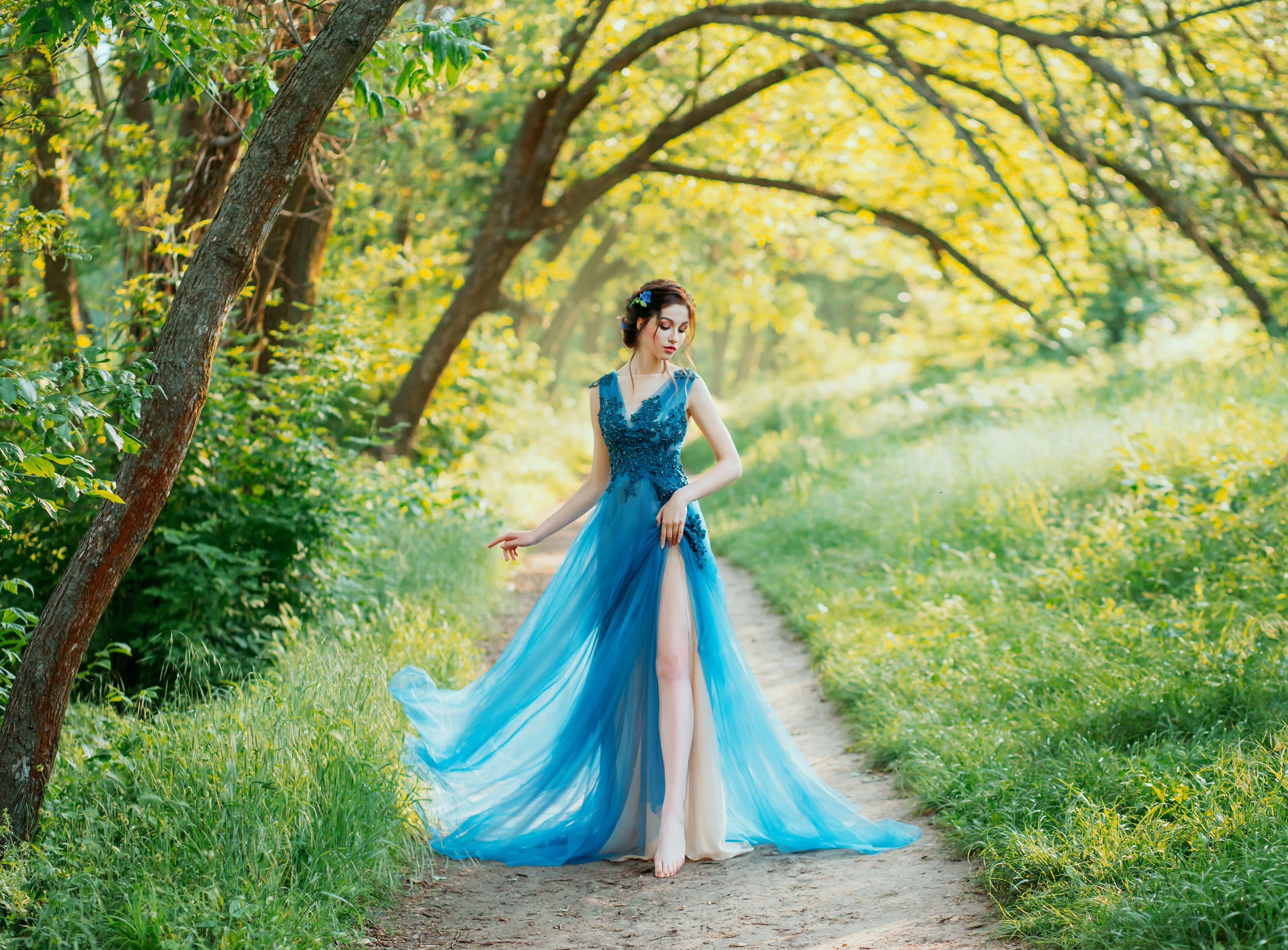 lonely sexy girl naked leg walk foliage green forest evening chic dress. hair decorated blue flowers of cornflowers. Elegant brunette hairstyle. sunny bright day nature summer spring wedding party art