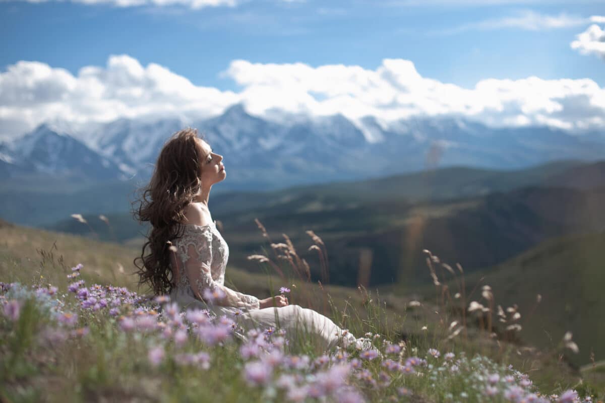 A lovely maiden in a gray dress sits on the mountain with wild purple flowers