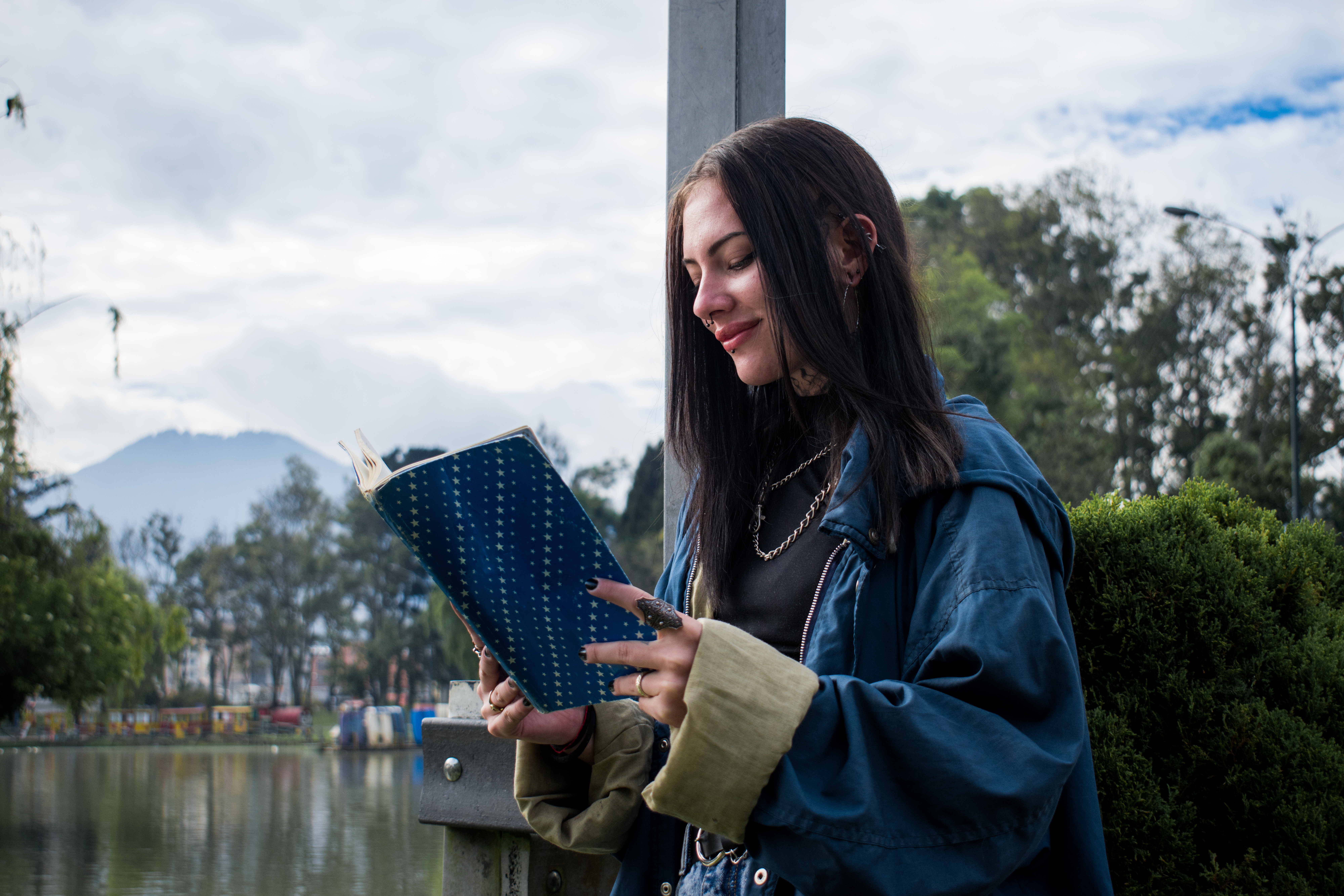 Young woman dressed in blue reading a book next to the lake.