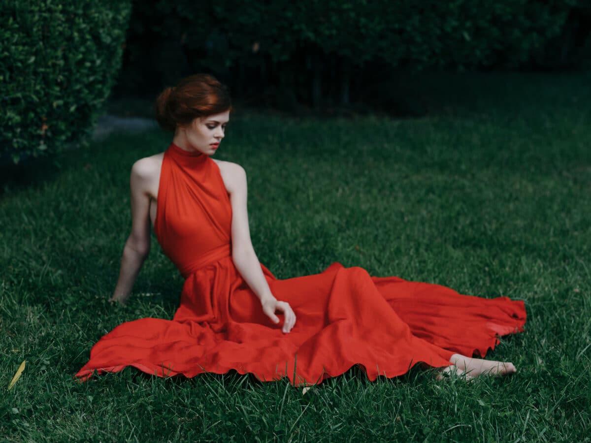 Woman in red dress sitting on the lawn in the garden charm