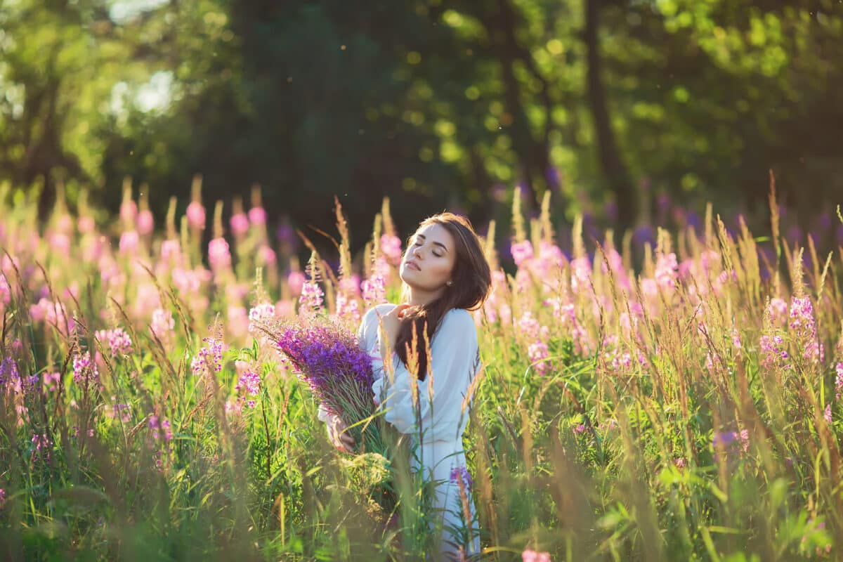 Beautiful young woman, holding lavender in a field on sunset.