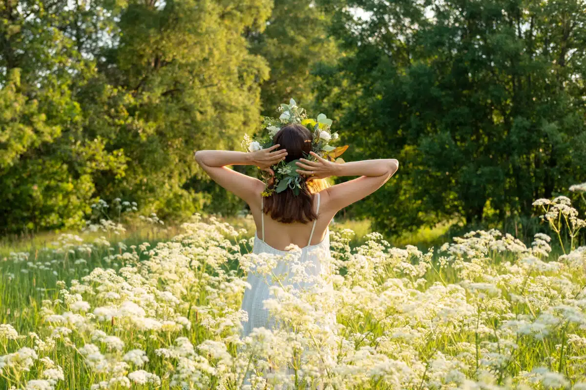 Beautiful brunette woman in flower wreath standing in the field in summer