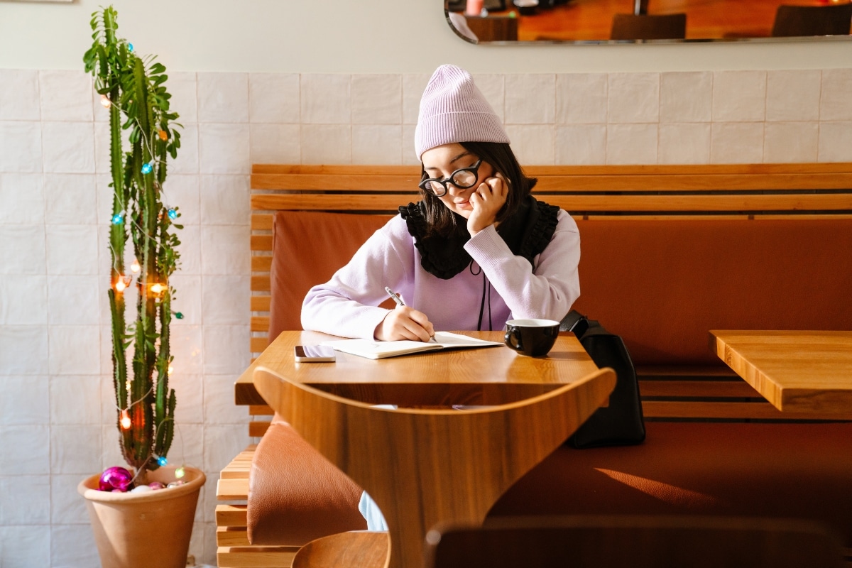 Young asian woman writing down notes while drinking coffee