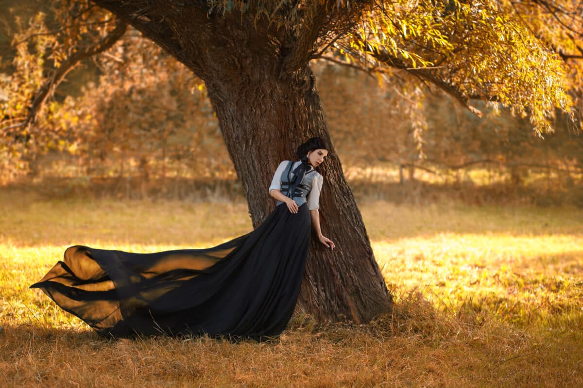 Exquisite lady in a vintage dress leaning against a tree in the garden