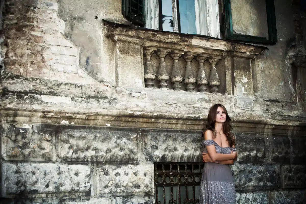a lonely young woman standing outside of the medieval stone house