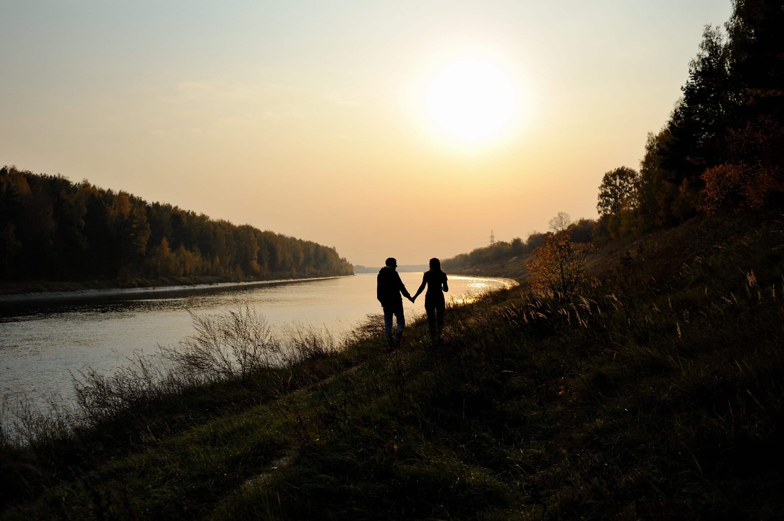 Young couple is walking along the river bank at sunset