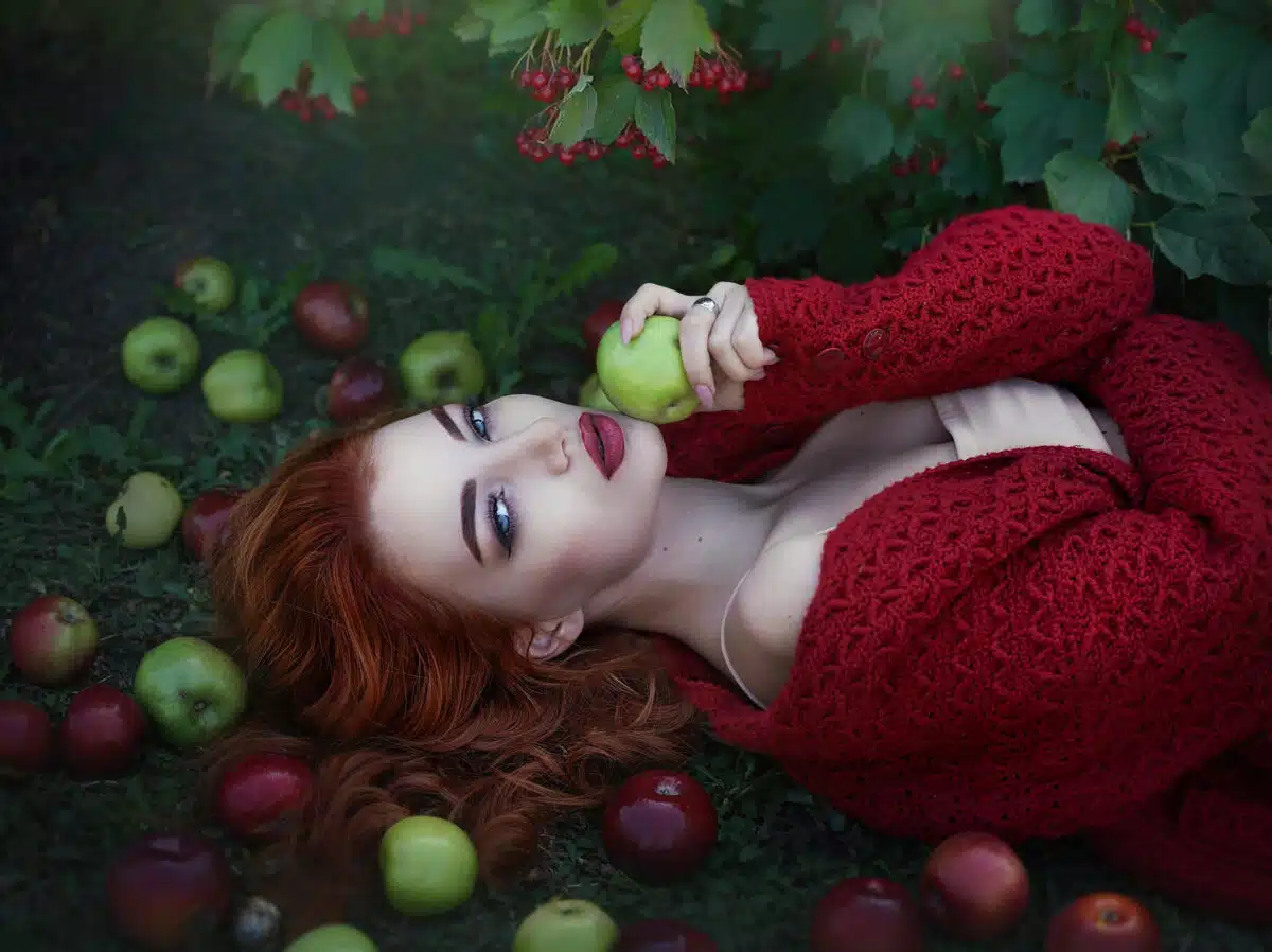 attractive beautiful red-haired woman lying on the ground with apples under the rowan berries