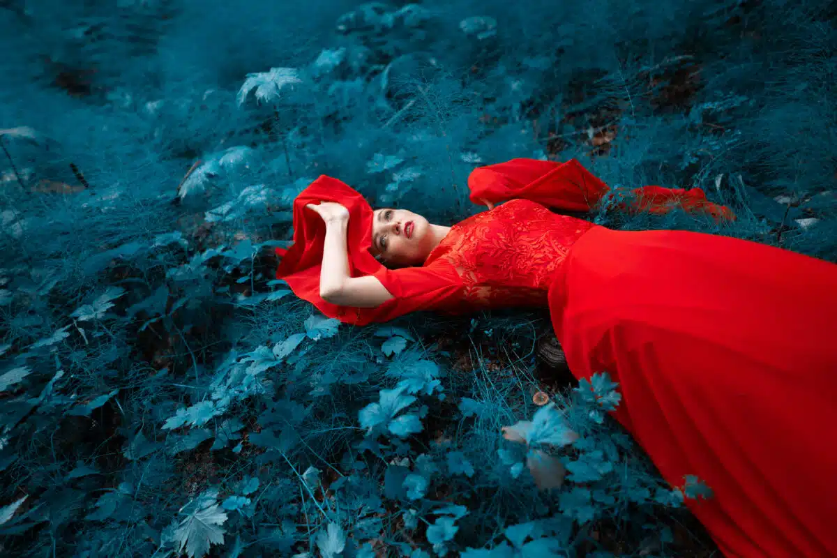 The girl lies in the grass in a red lava dress