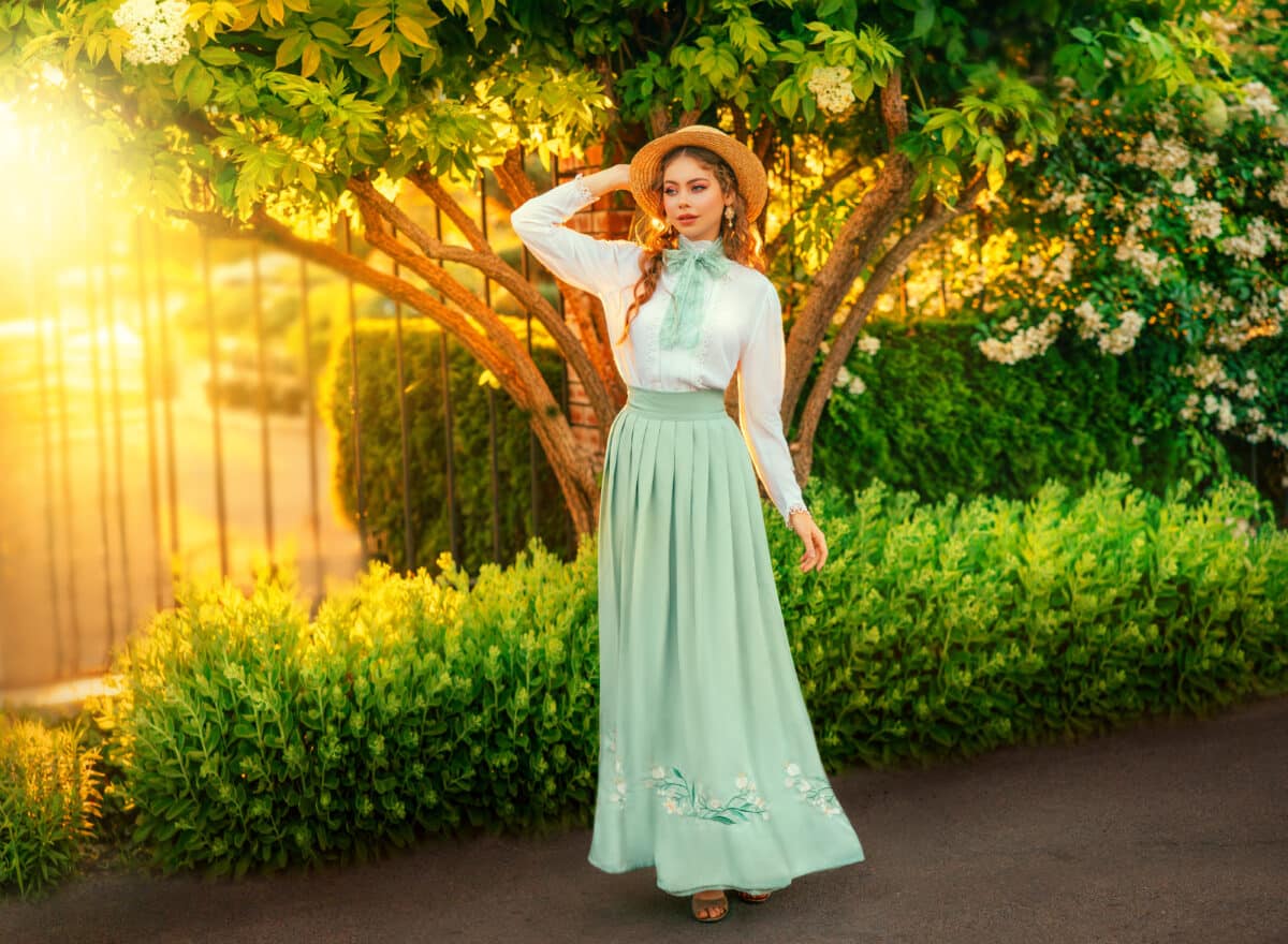 Art Fantasy young woman in vintage straw hat on head walking in garden, girl princess pretty face red hair, retro old style white blouse mint skirt, bow tie. green grass yellow sun light summer nature