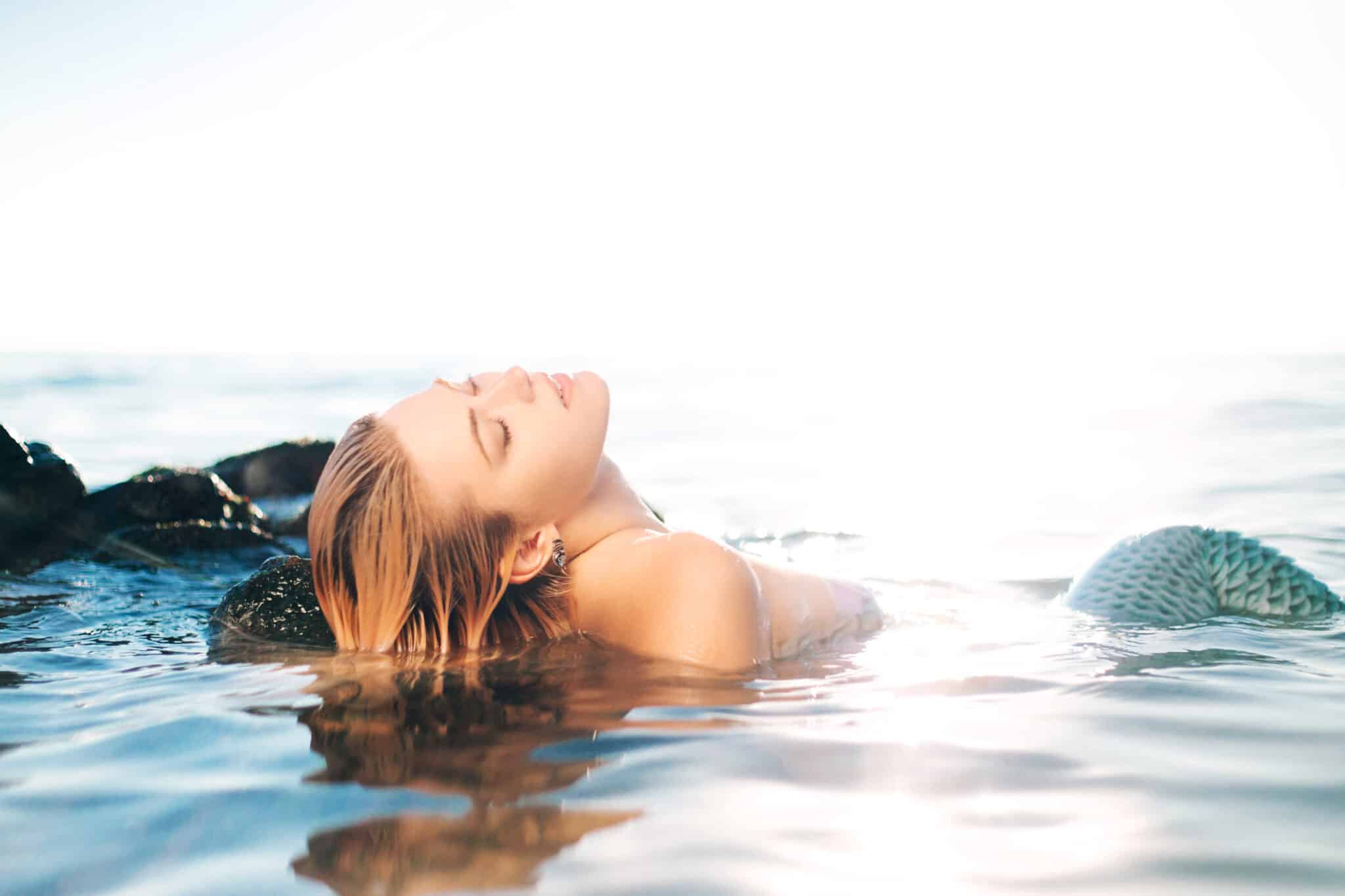 blonde mermaid lying in the shallow sea water eyes closed