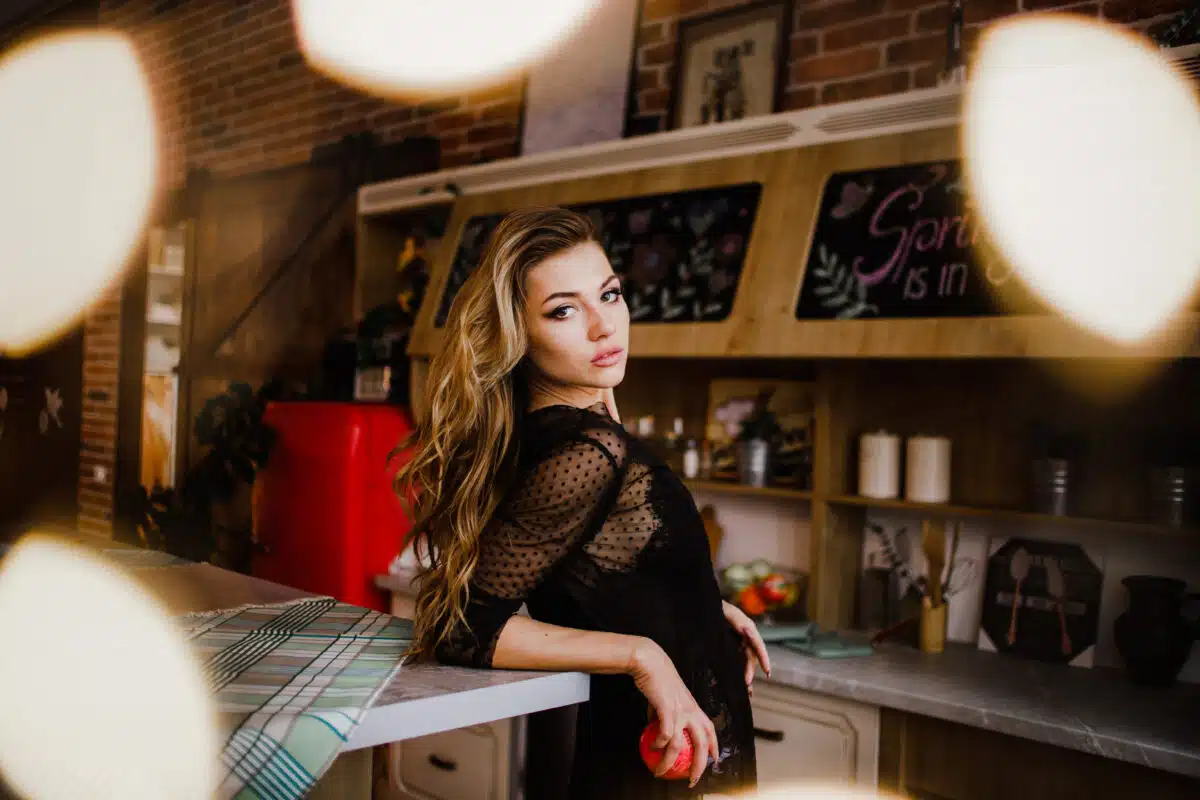 alluring lady in black stands at the counter with a red apple in her hand