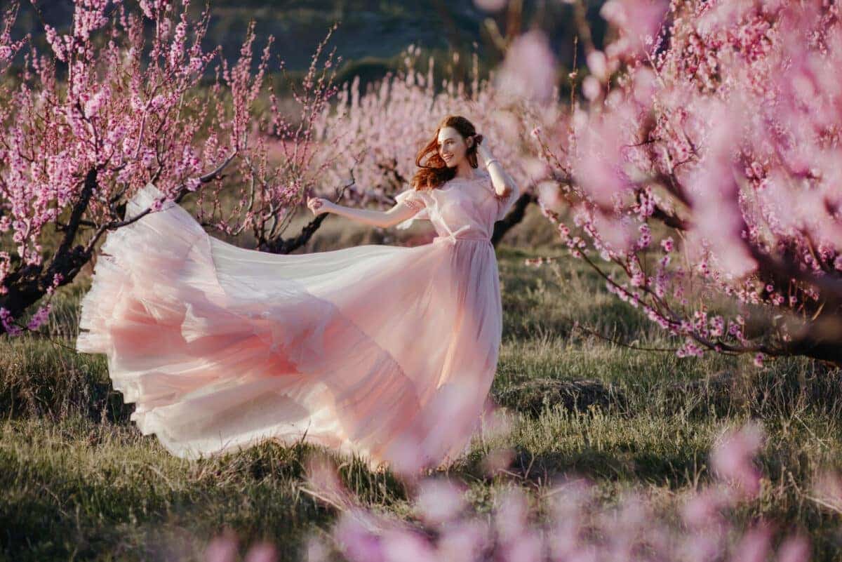 beautiful lady fairy in flowy pink dress enjoying the pink spring blooms in the garden