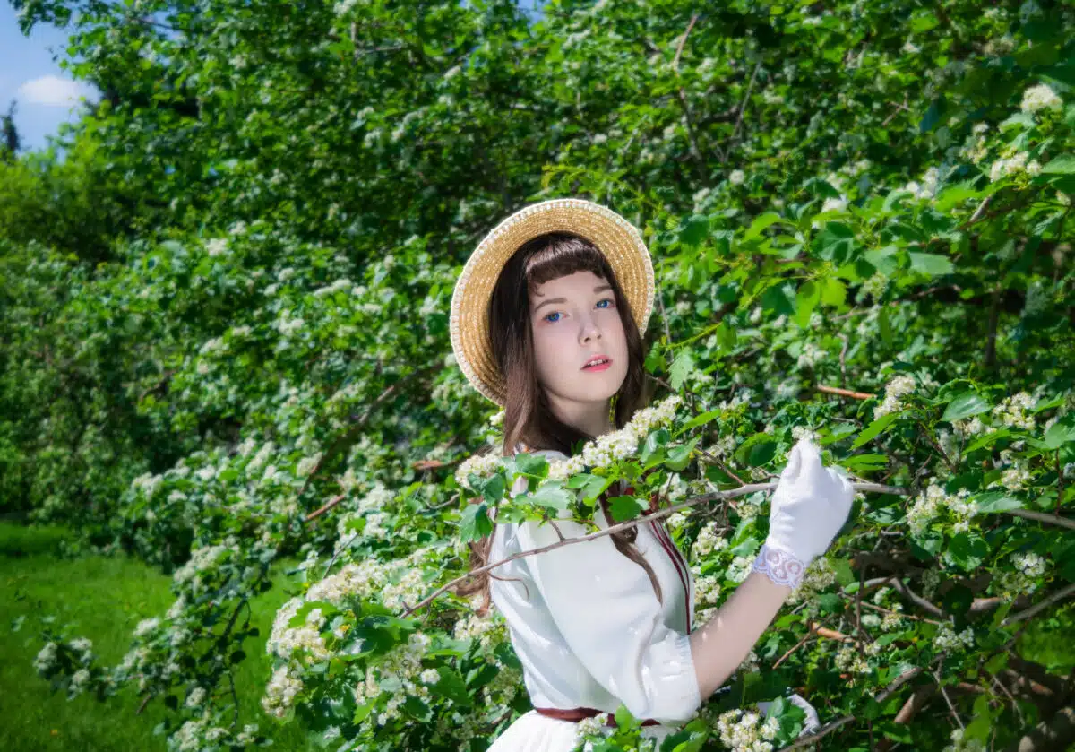 girl in a white dress and straw hat standing next a bush