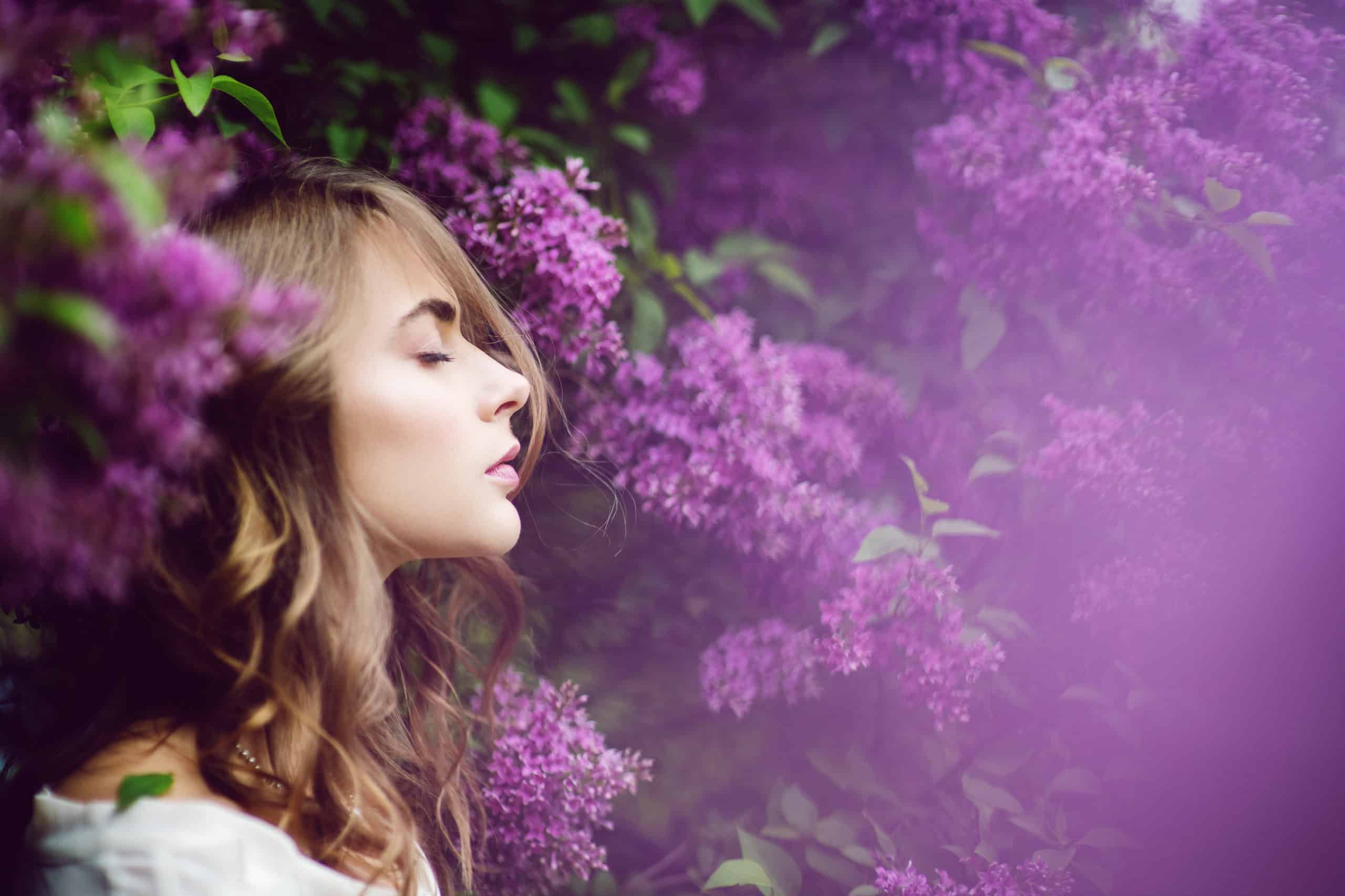 Beautiful young woman with closed eyes surrounded by lilac flowers.