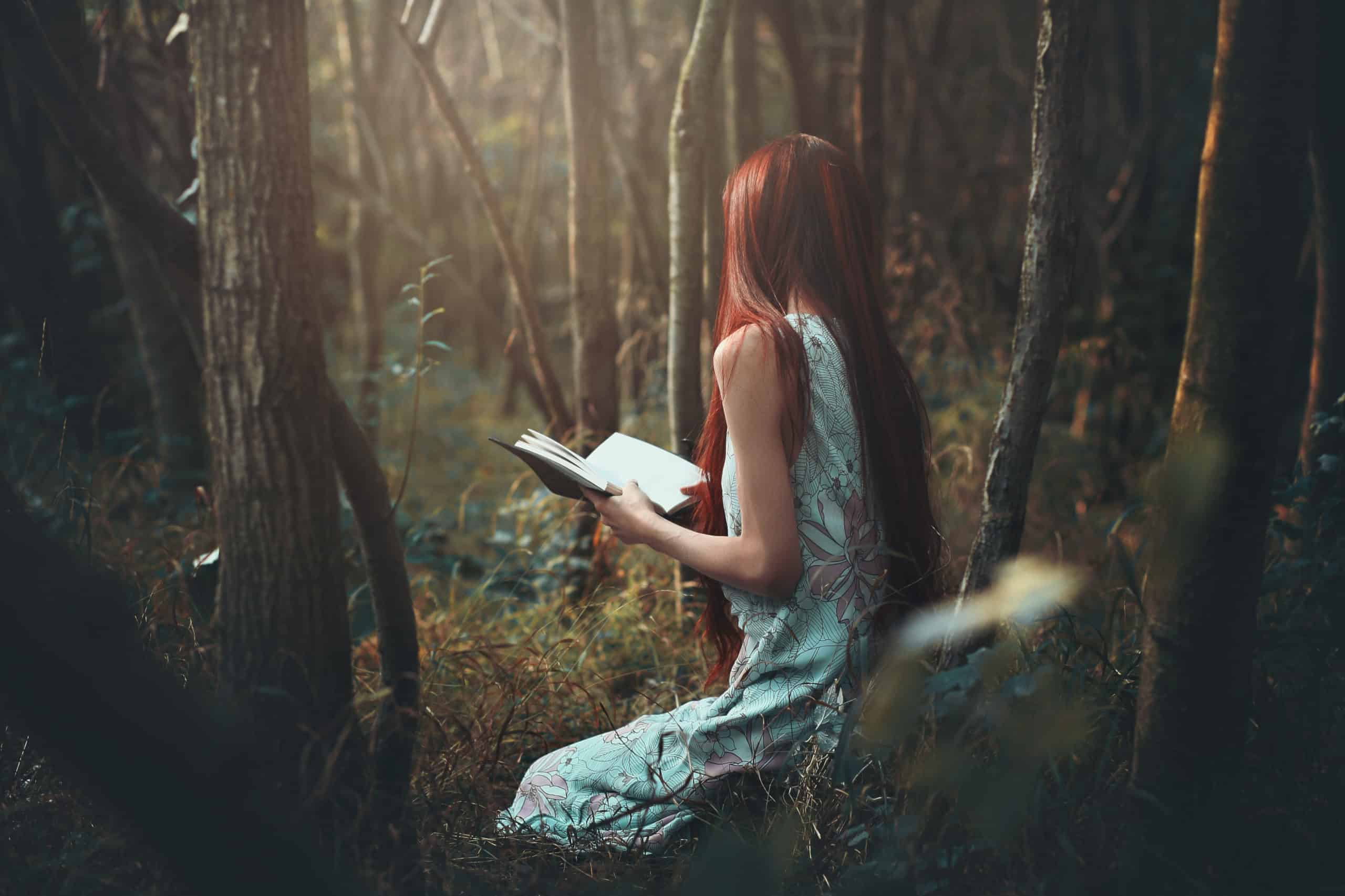 Woman in blue sleeveless dress with long hair reading alone in the woods.