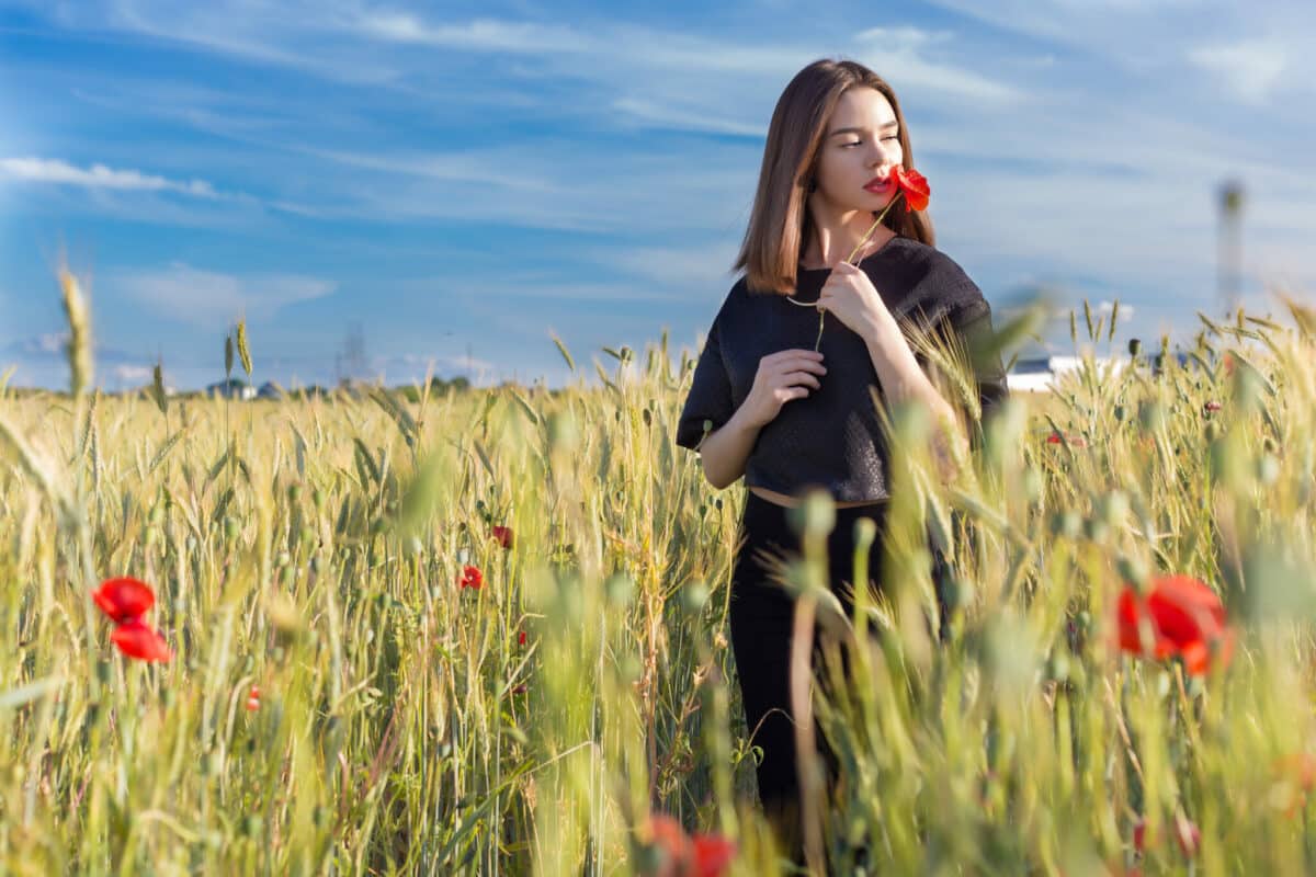beautiful woman in black holding a poppy flower in the field