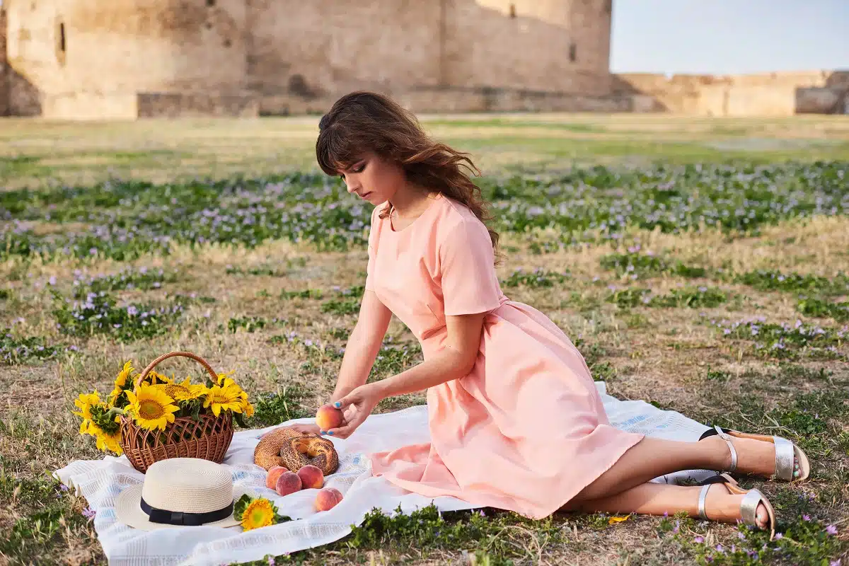 a beautiful woman having a picnic with peaches on the grass on castle grounds