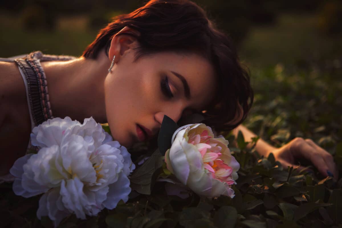 Beautiful brunette woman with eyes closed resting with the lovely flowers in nature