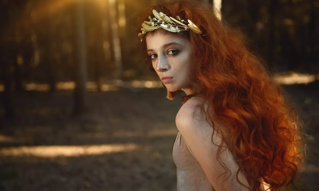 Enigmatic red haired woman in woods.