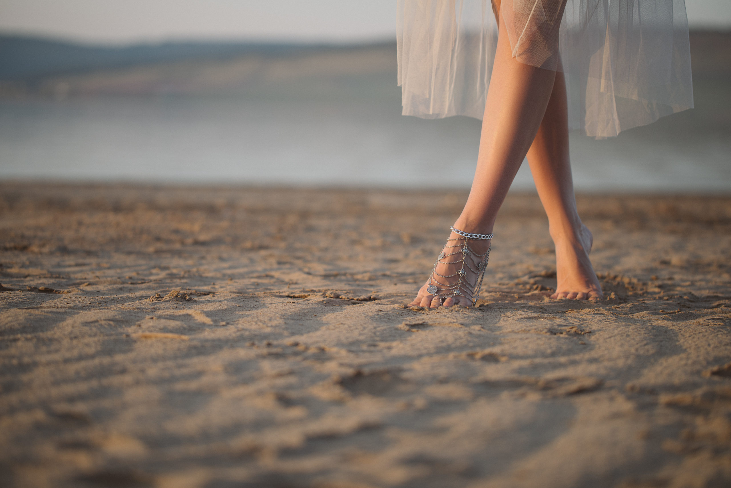 Legs of a woman in white dress enjoyong the sand on the beach.