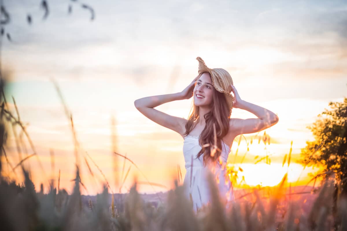 a carefree beautiful girl in the white dress with hat in a wheat field at sunrise
