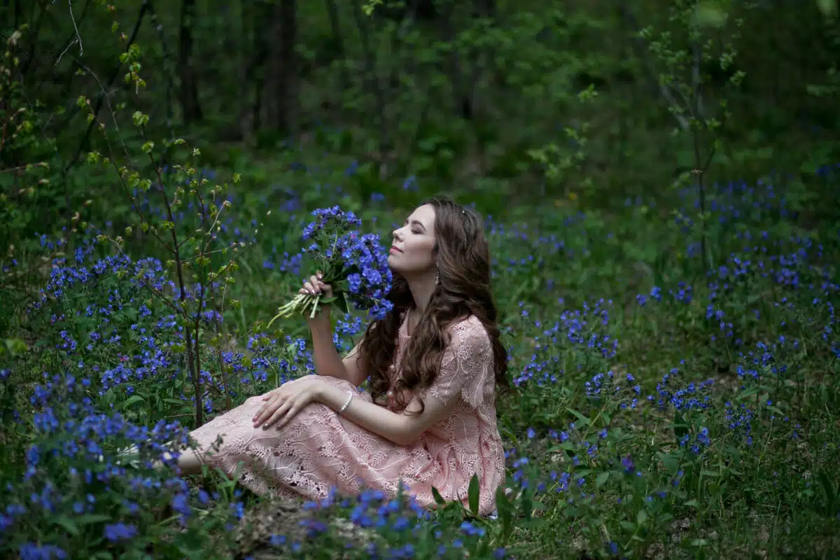 A young girl walks in a field of blue flowers at dusk.