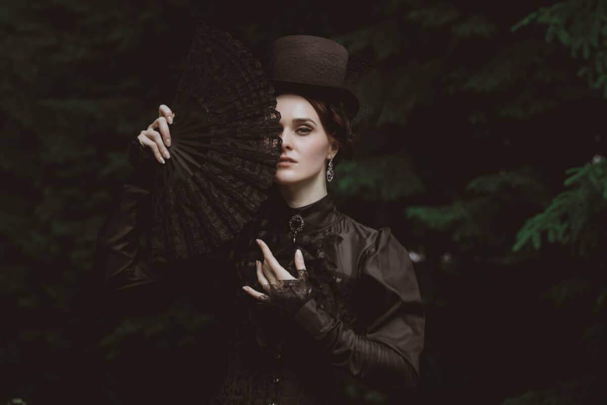 a young lady in black dress covering her face with a black fan