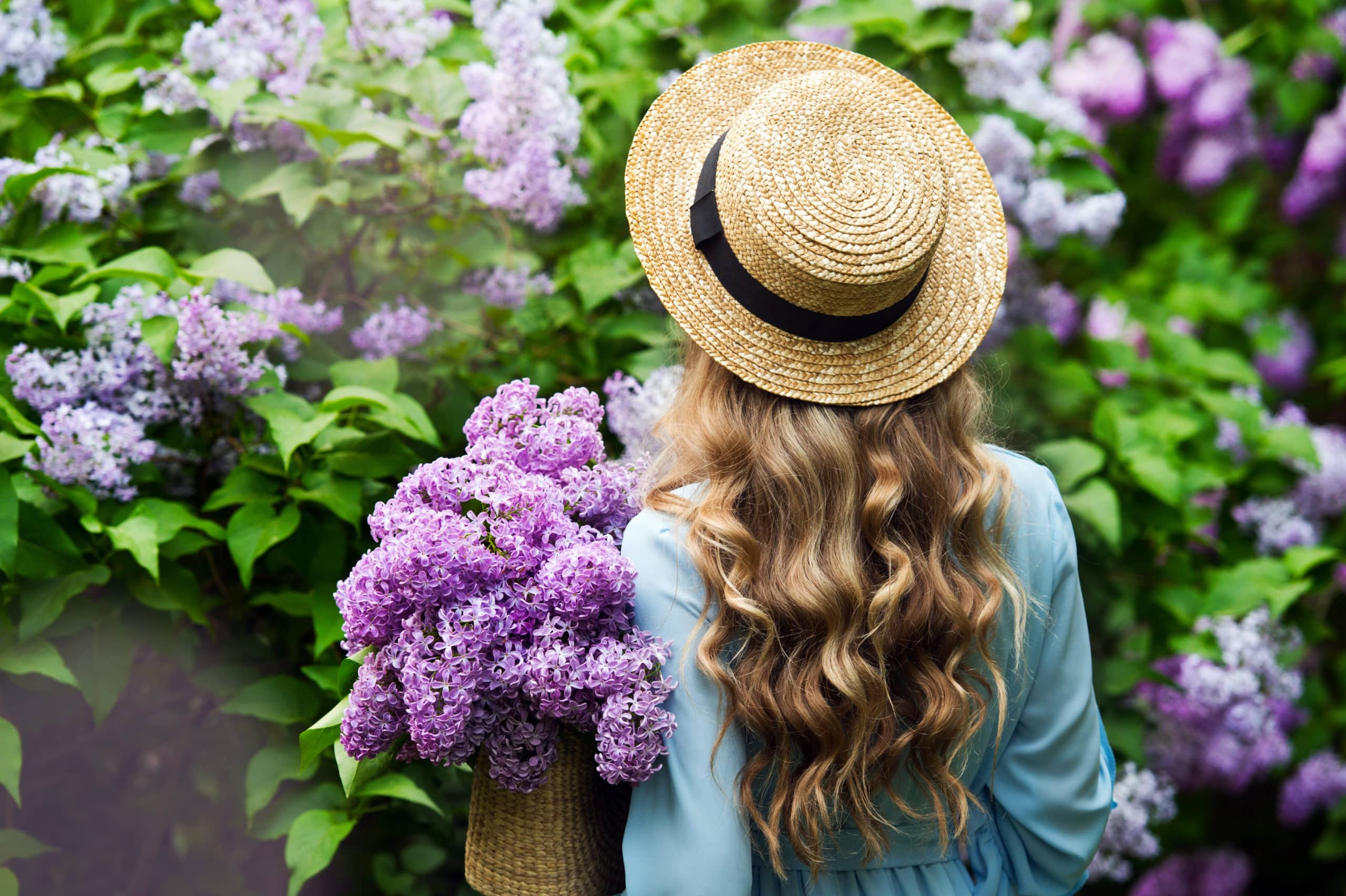 Beautiful girl in straw hat in lilac garden.