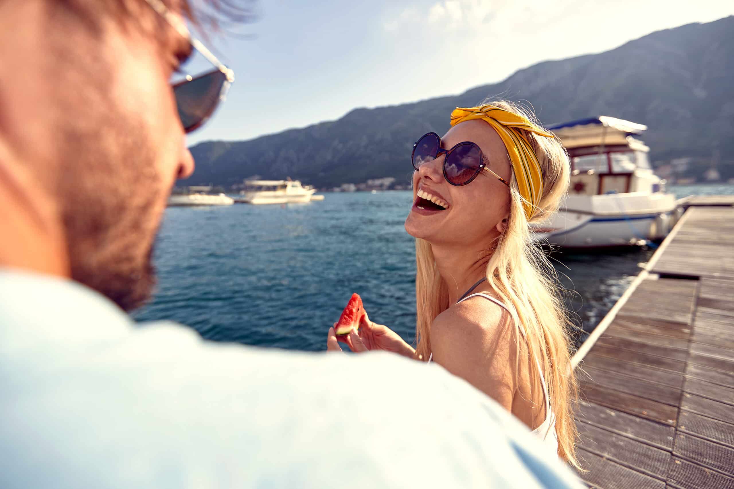 at a dock, a beautiful smiling blonde holding sliced watermelon and looking at her lover