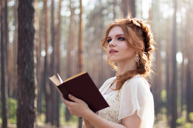 Red-haired girl in vintage style reads a book in the woods