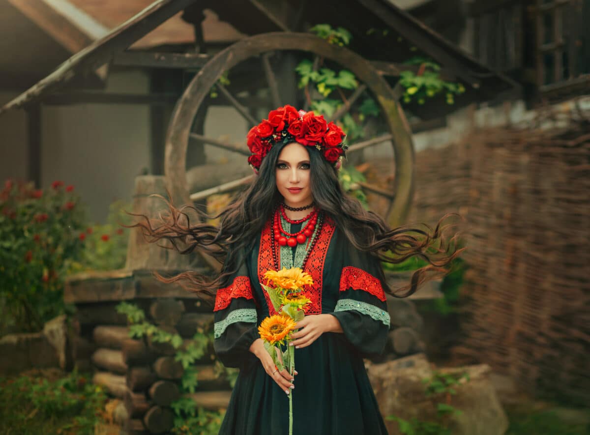 Close-up portrait Ukrainian happy girl looks at camera. Authentic woman smiling face. National ethnic vintage costume black dress stylish vyshyvanka. Wreath crown on head red flowers roses, poppies
