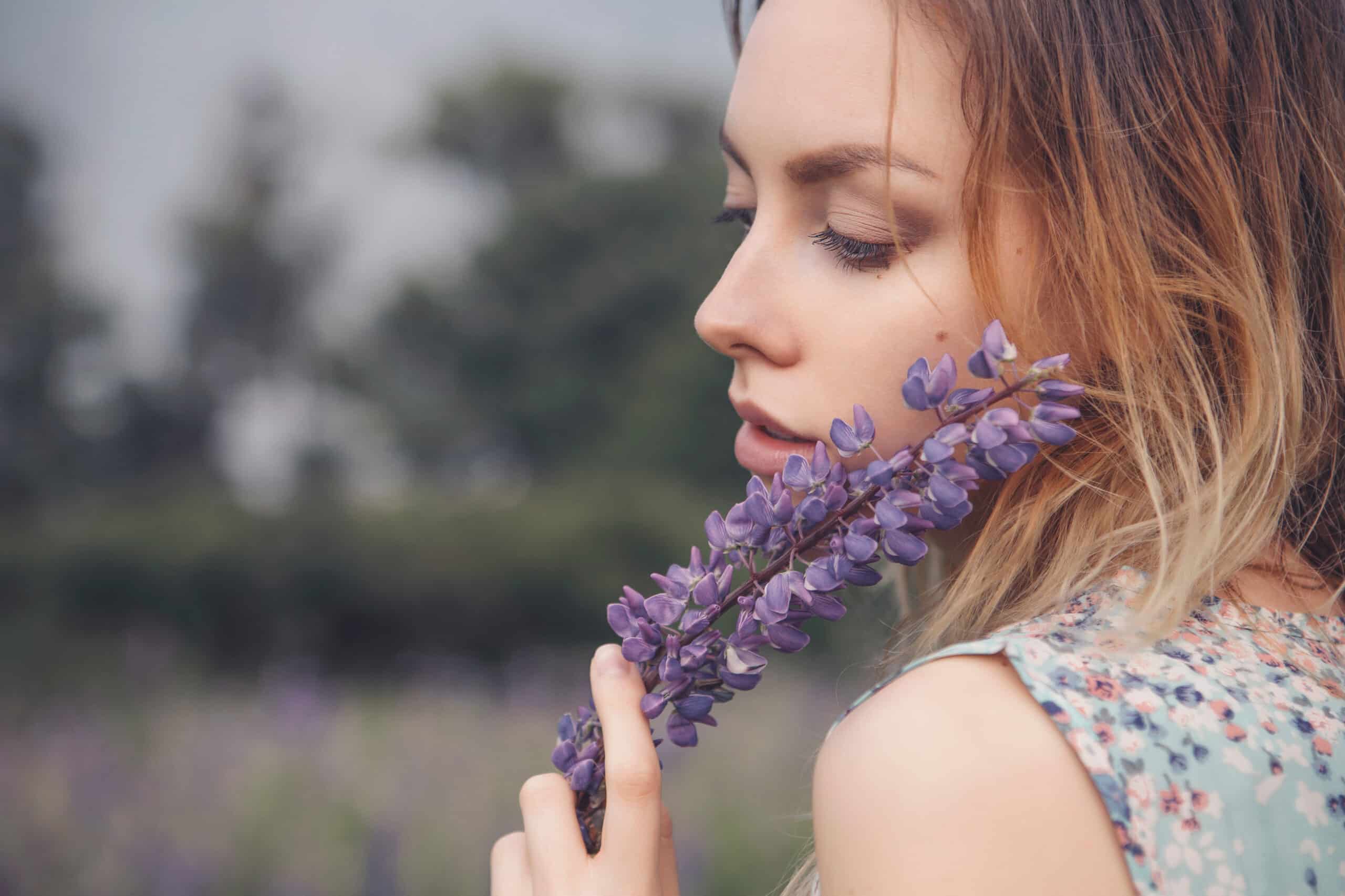 Beautiful brunette woman holding lavender flowers against her flawless face outdoor