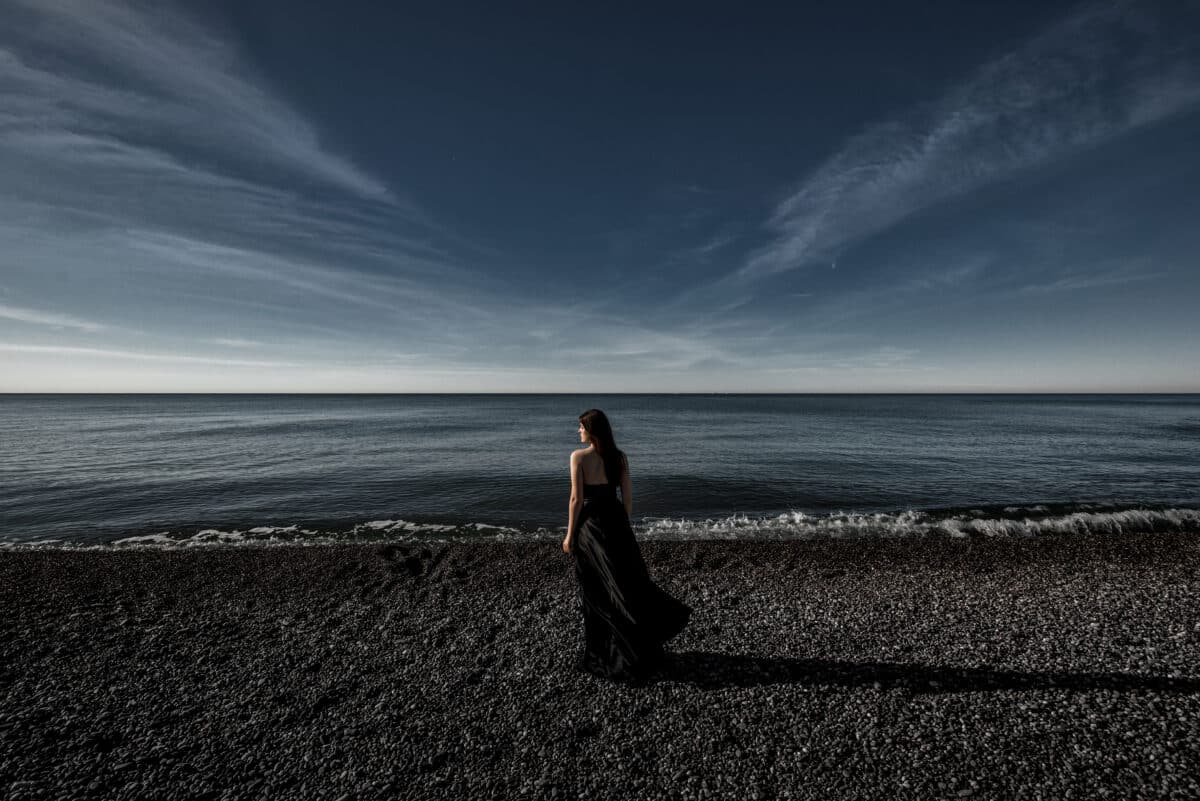 mysterious lady in black standing on the shore with stunning view of the ocean and the sky