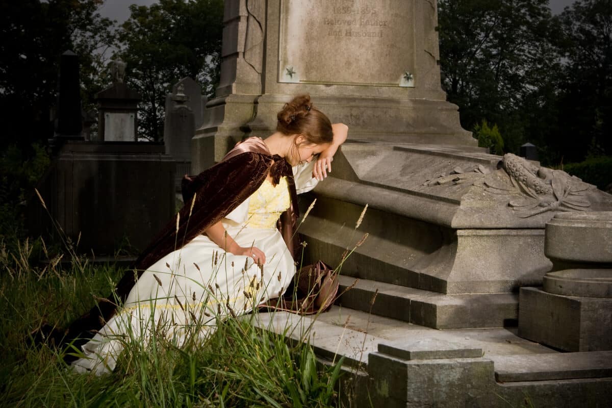 young woman in vintage dress mourning on a tomb