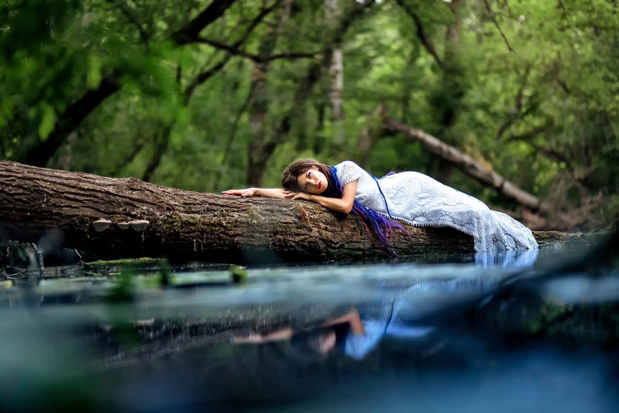 a girl in a white dress lying on a log in the water