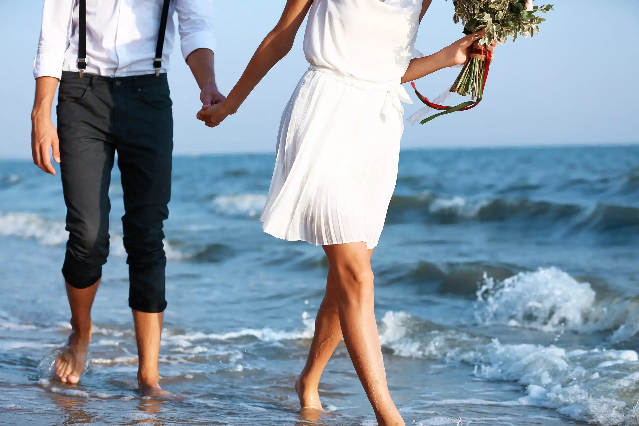 Young happy couple with flowers walking on seashore