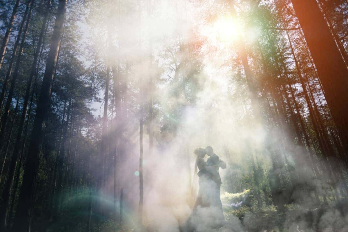 couple standing in the smokey woods with sun rays