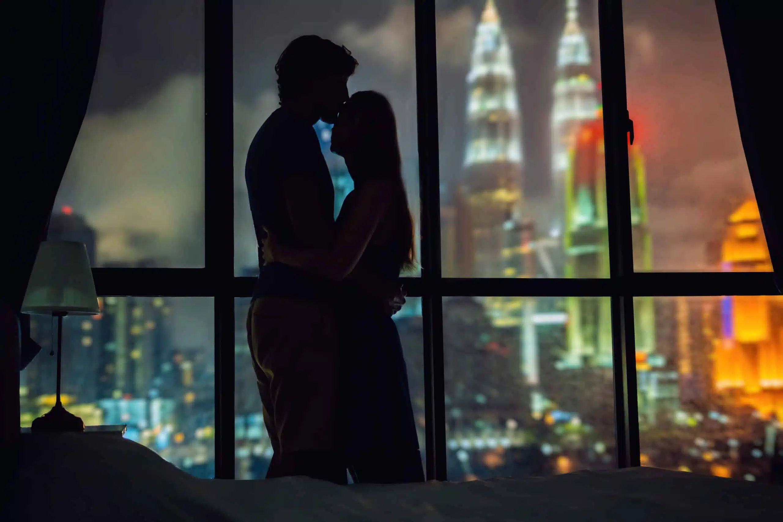 Silhouette of a loving couple against a window with a view of the night city