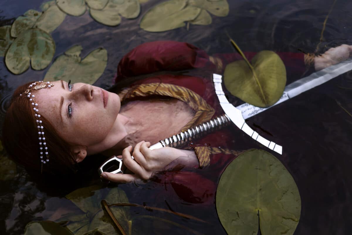 mysterious sad red haired girl in medieval dress with sword lying in the water with lilies