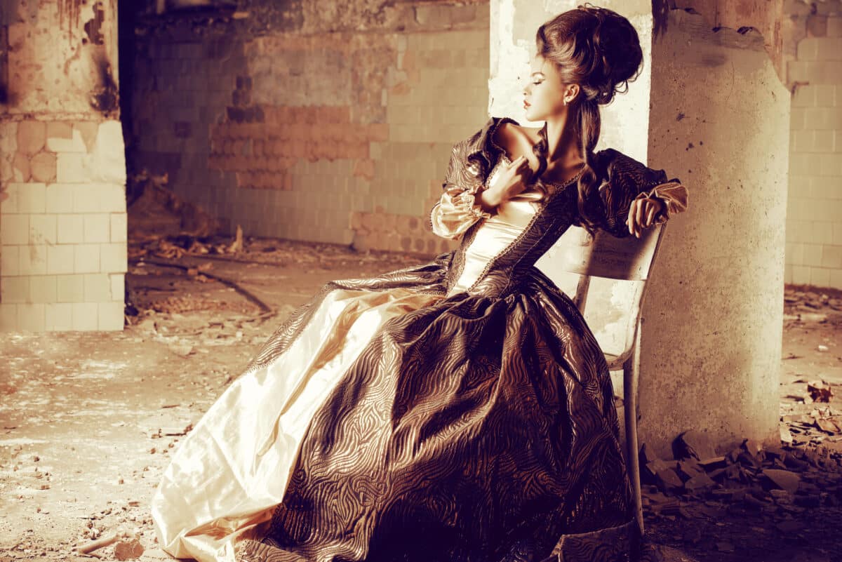 beautiful young woman in elegant historical dress sitting in the ruins of the castle