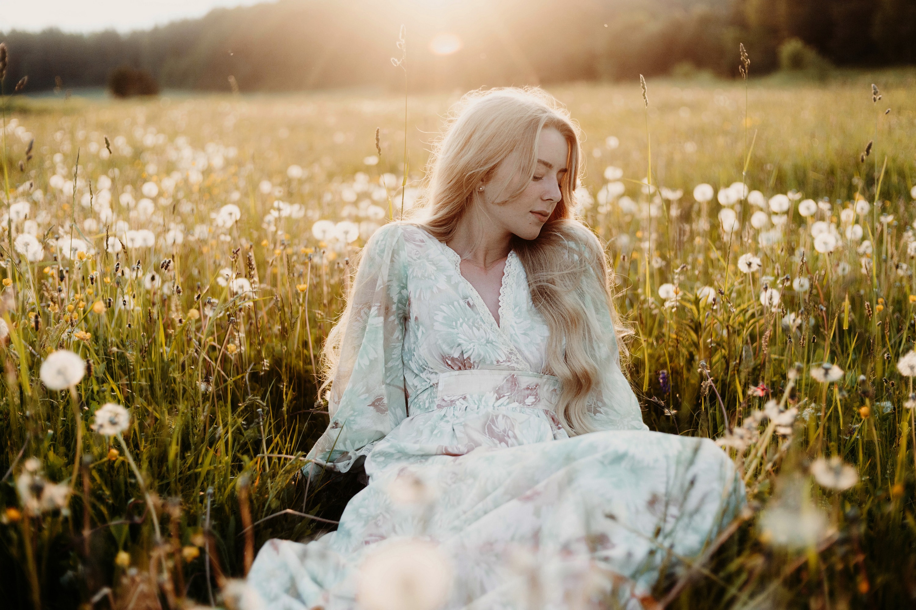 beautiful long-haired blonde in a dress in a field with dandelions