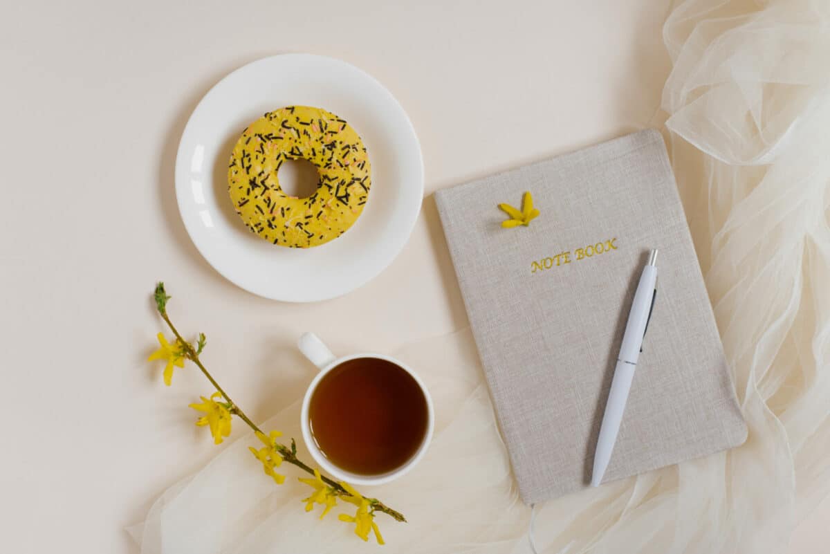 Notepad planner for business work with hot tea, a composition of flowers and donut on a beige background