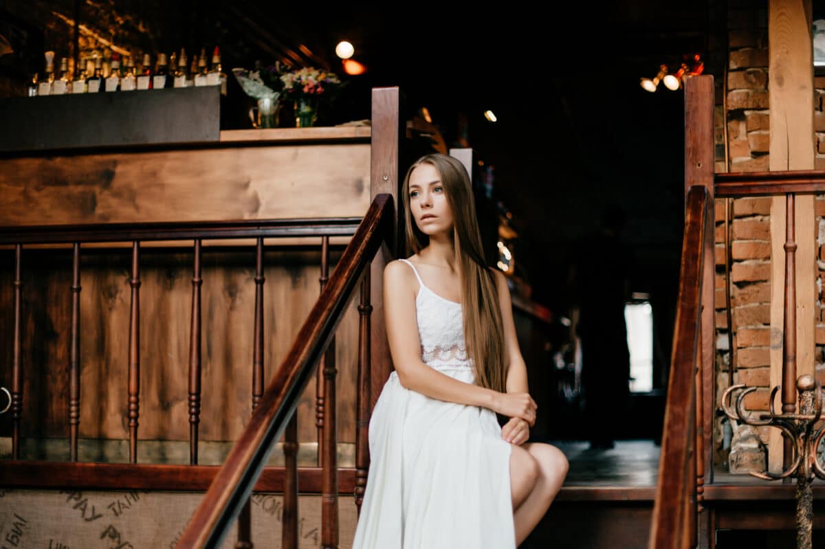 Young romantic thoughtful lady in a long white dress sitting on the wooden stair
