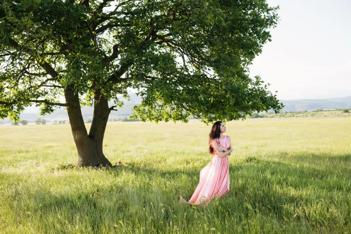 princess in a pink dress enjoying the green nature and the shade of the giant oak tree behind her