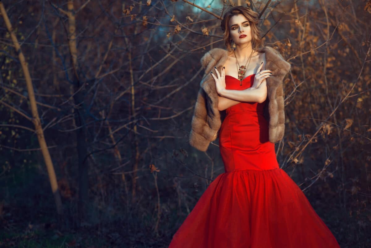 Gorgeous woman in a fiery red dress with updo hair standing in the woods