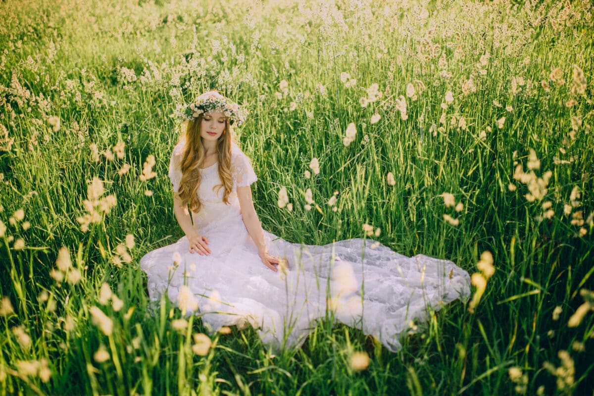 Young girl in a white dress in the meadow. Woman in a beautiful long dress posing on a meadow. Stunning bride in a wedding dress